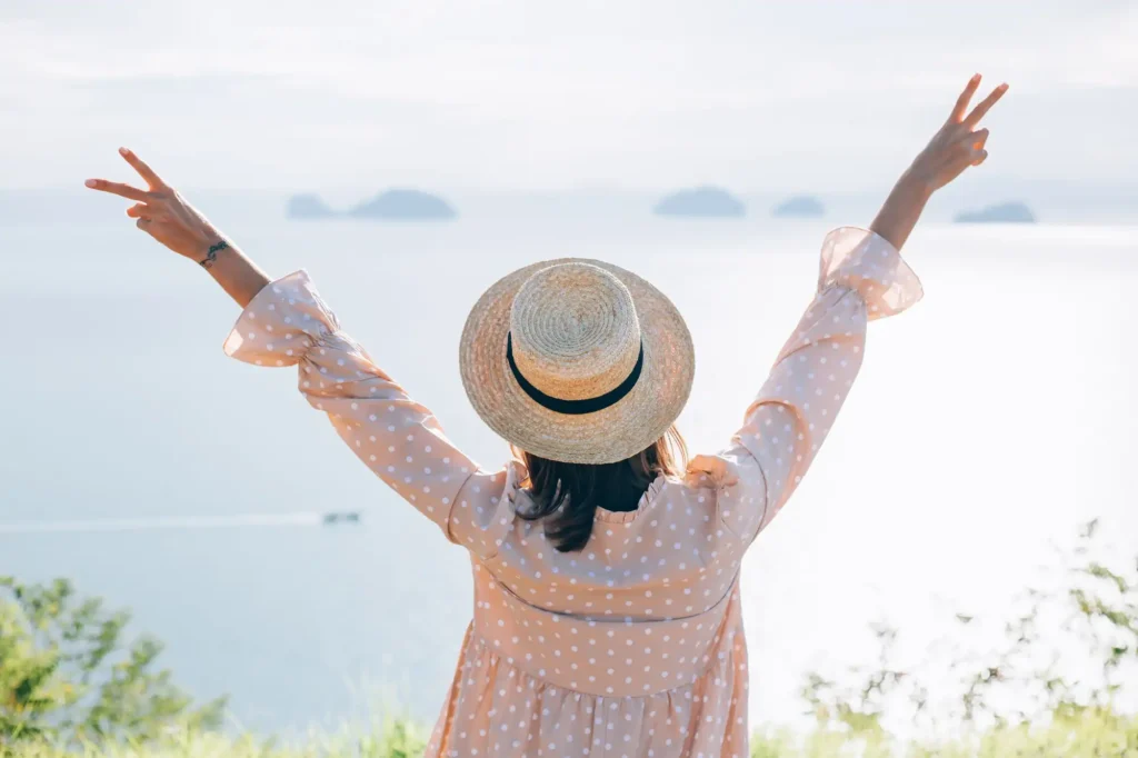 In the image a girl with her arms to the sky as she admires the sea