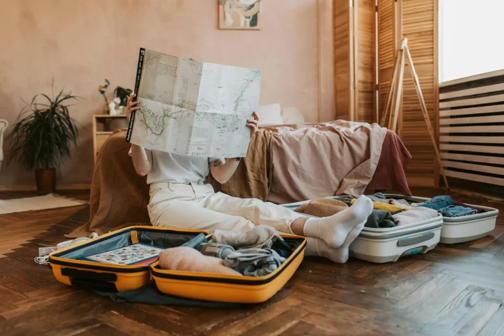 In the image a girl packing her bags and planning her trip with a map